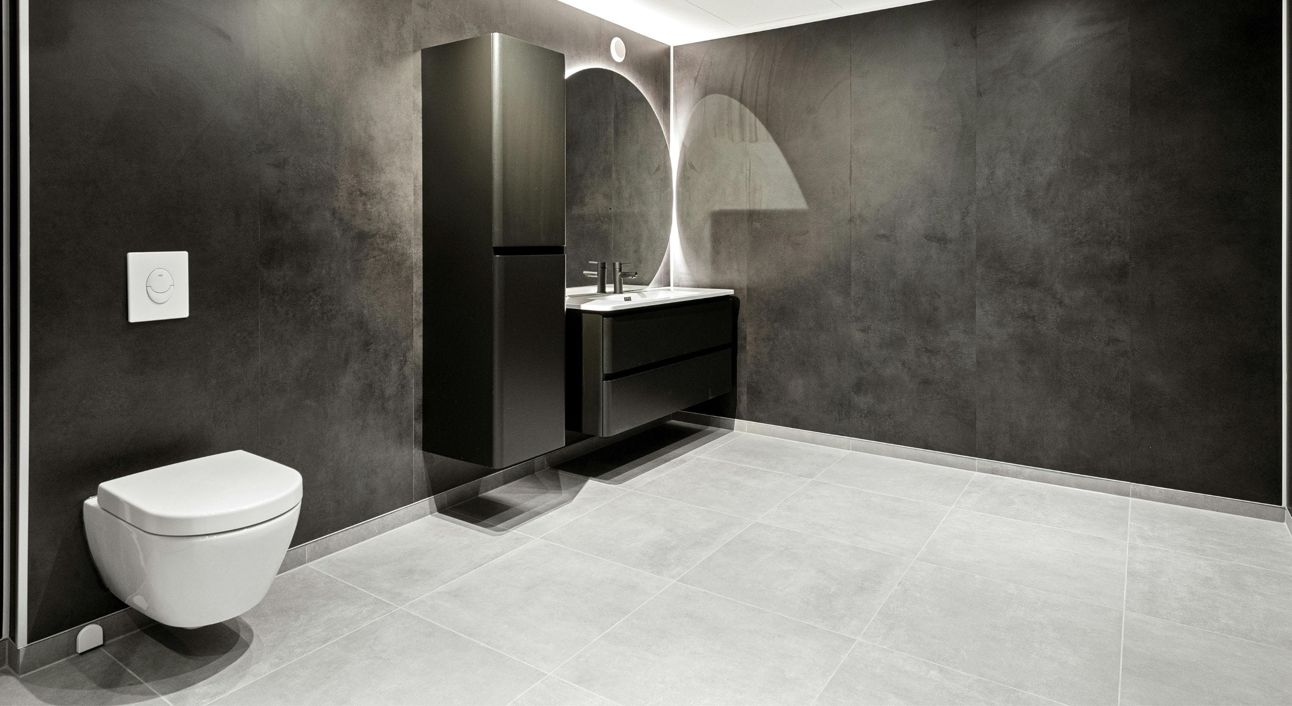 Baño con inodoro suspendido, pulsador empotrado y porcelánico gris de gran formato