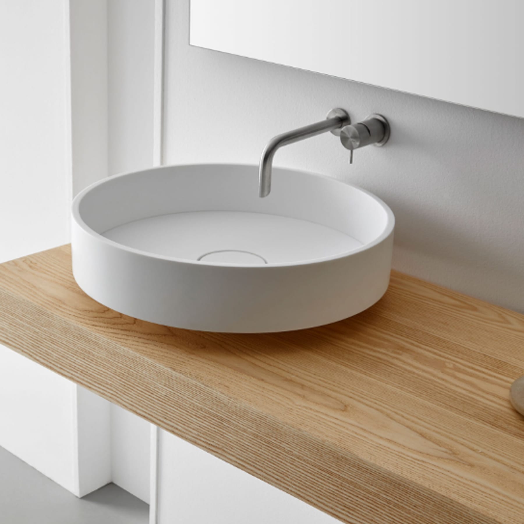 Lavabo sobrepuesto redondo blanco sobre encimera de madera con grifo mural