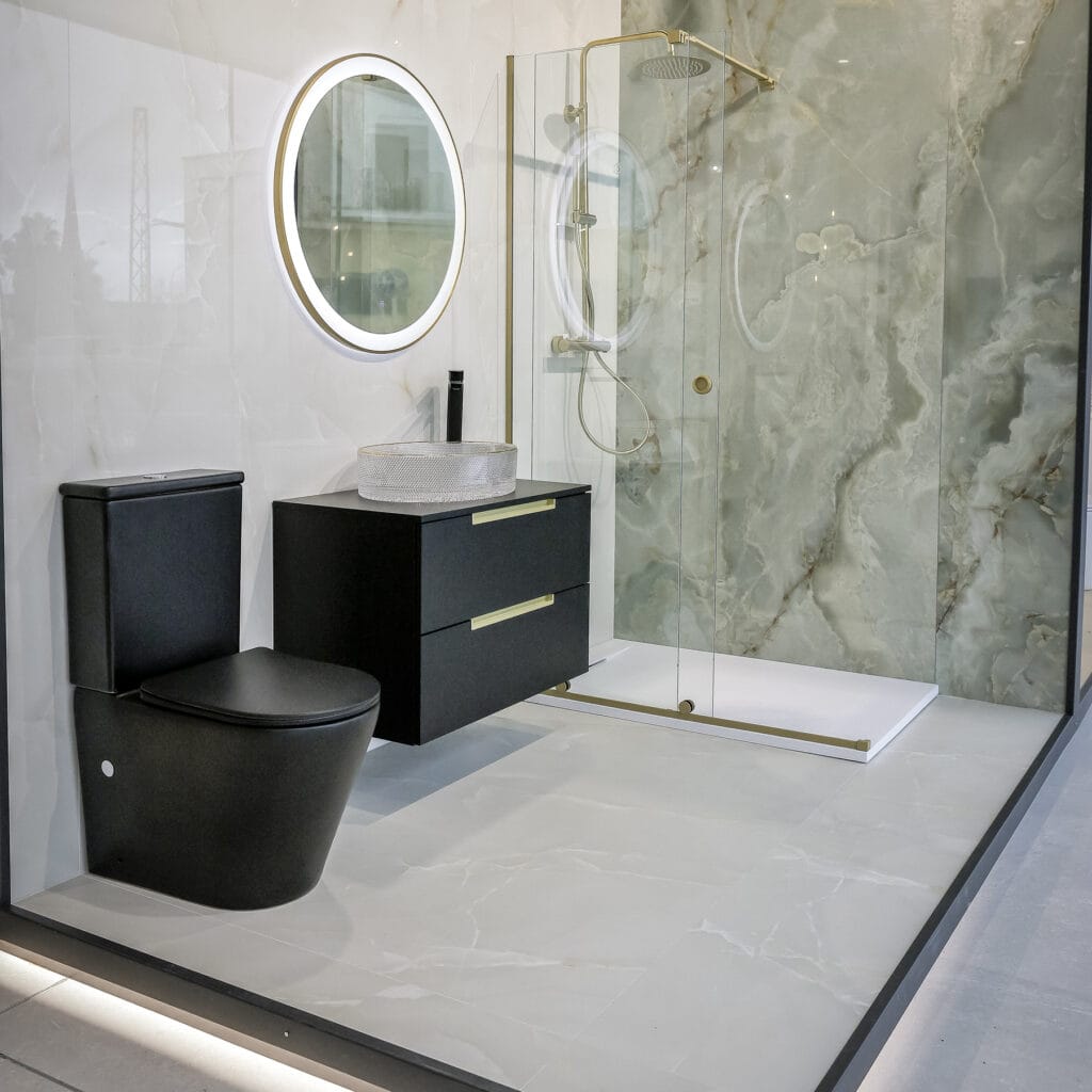 Baño del showroom con inodoro negro, espejo redondo iluminado y ducha de mármol verde