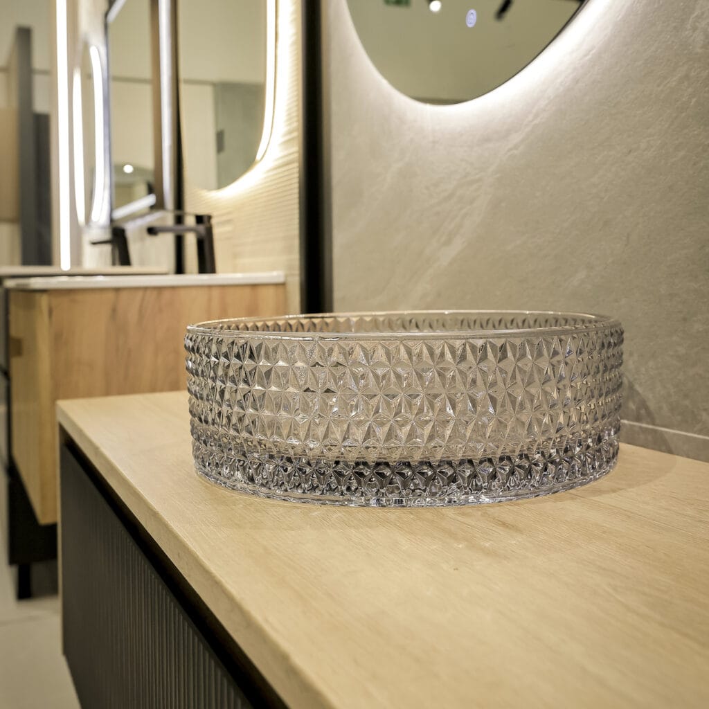Lavabo de cristal facetado sobre encimera de madera con espejo redondo